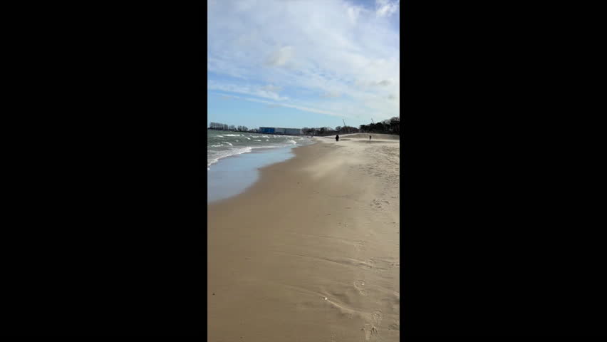 
strong wind carries sand to the sea in Gdansk, people walking along the sea in Gdańsk on a windy day