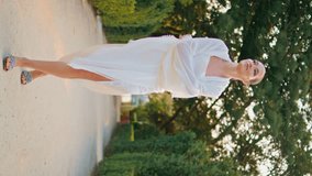 Gorgeous girl going on alley with ancient marble sculptures. Elegant smiling woman walking at pathway green garden vertically video. Carefree lady strolling park wrapped in white cloth at evening. - Powered by Shutterstock - Get 15% off with code: PIKWIZARD15