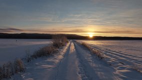 A drone shot of the car tracks on a trail in a vast snowy field with mountains in the background at sunset in Toutsi village, Otepaa, Valga, Estonia - Powered by Shutterstock - Get 15% off with code: PIKWIZARD15
