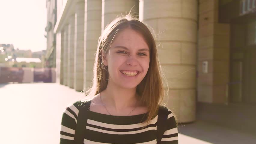 A young Caucasian teen girl laughs and smiles looking at camera, close-up outside. Optimistic teenage girl with friendly expression.