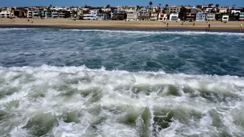 An approaching drone shot of South Bay in Los Angeles, CA capturing sun-kissed beaches, rolling waves, and blazing sunshine.
