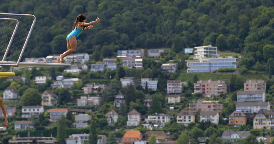 Child jumping off a diving platform into the lake, mid-air in slow-motion at 800 fps, with a scenic background of houses and trees, capturing the adventurous spirit and thrill of a daring leap