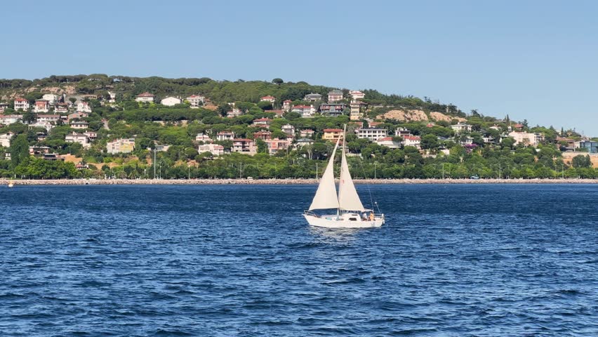 White sloop rigged yacht sailing in Marmara Sea at sunset. Sailing ship in full sail off the coast of Prince Islands of Istanbul City. Yachting at windy day. Sailing boat video. Sailboat
