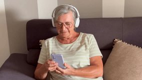 Close up relax peaceful mature woman listen music leaned on sofa, holds phone enjoy quality sound through wireless headphones, feels serenity resting on pastime alone at home. Modern tech, relaxation - Powered by Shutterstock - Get 15% off with code: PIKWIZARD15