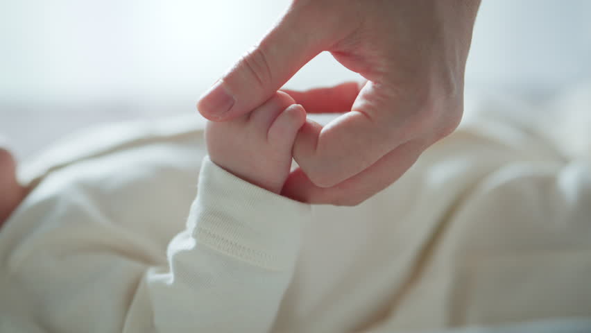 Close-up little hand of child baby holding hand of mother, A newborn holds on to mom's, dad's finger, Love and relationship with infant, Care and support, Dreaming and protection
