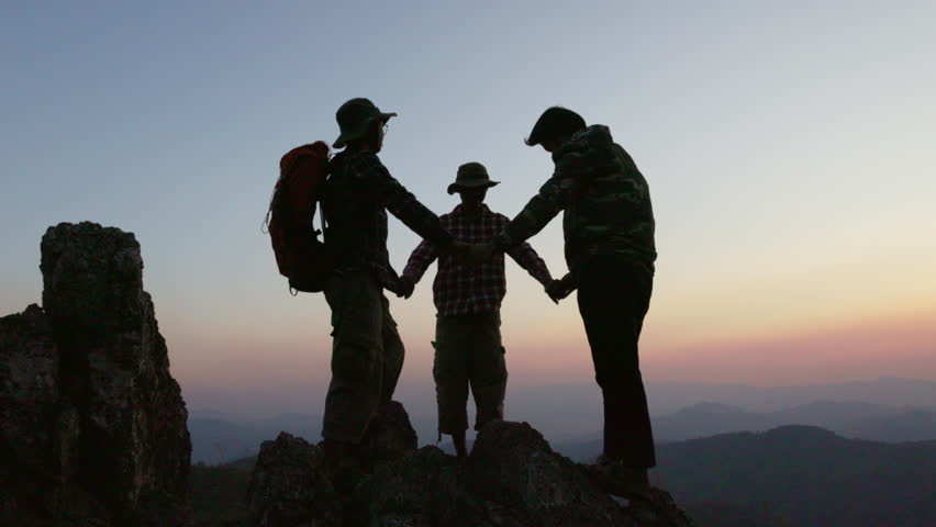 Silhouette of a group of climbers holding hands on a mountaintop represents unity and teamwork, success concept.