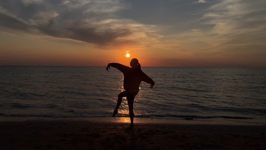 The silhouette of a girl dancing on the sand against the background of sunset and the horizon of the sea. 4k video. High quality 4k footage.