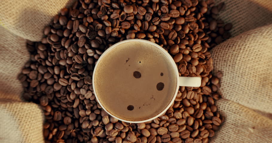 Coffee, above and cup with beans at cafe for strong caffeine, latte or cappuccino on table. Top view or closeup of mug, brew or liquid with brown froth for mocha, espresso or breakfast beverage