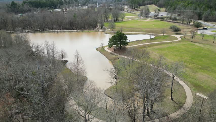 A drone view over a muddy pond surrounded by fields and leafless trees