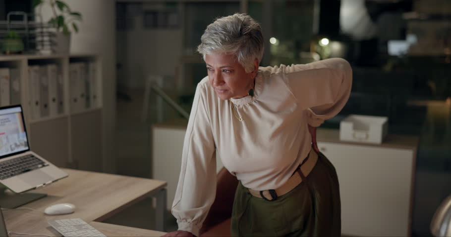 Anatomy, back pain and posture with mature businesswoman in office at night for project deadline. Burnout, desk and health of design employee in workplace with accident, emergency or spine injury