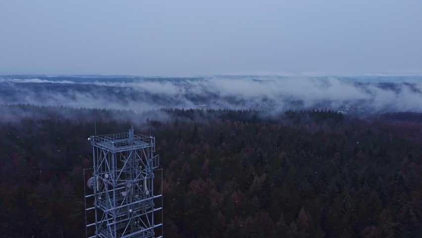 Communication tower above a misty forest in light snow