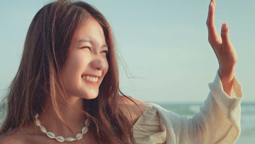 Happy young asian woman with freedom on the sea beach at golden sunset, woman playing sunlight with hand, Female tourist on seaside summer vacation.