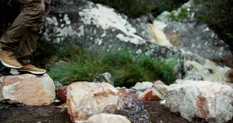 Person, feet and rocks for hiking outdoor with water path, travel journey and trekking adventure of fitness. Hiker, legs and walking on stone for mountain trail, balance exercise and nature challenge