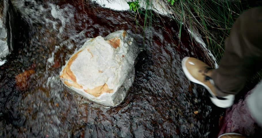 Feet, rocks and person for hiking stream with water path, travel journey and trekking adventure of fitness. Above, legs and walking on stone for mountain trail, balance exercise and morning outdoor