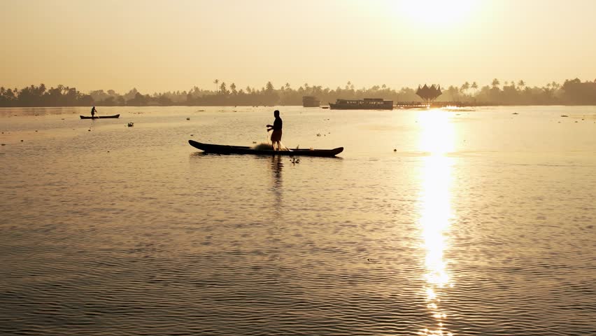 Fisherman pulling a net from a wooden boat, silhouette against beautiful sea horizon at sunrise with sun rays. Kerala, India. Traditional fishing.