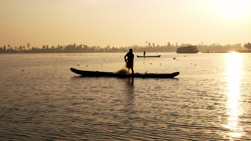 Fisherman fishing from a wooden boat, at sunrise with sun rays. Kerala, India. Vacation Concept. Alleppey.