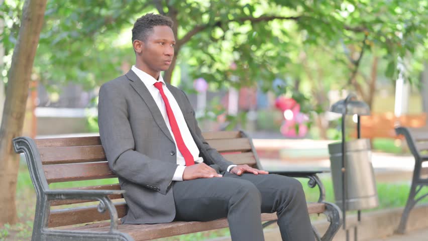 Thumbs Down by African Businessman Sitting on Bench