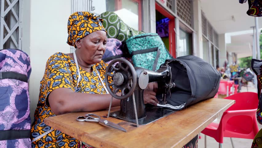 African woman spinning manual wheel of sewing machine working outdoors