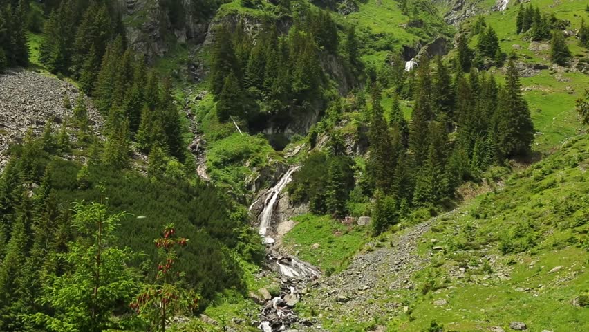 The beautiful foamy waterfall coming down the rocks on the green mountainside