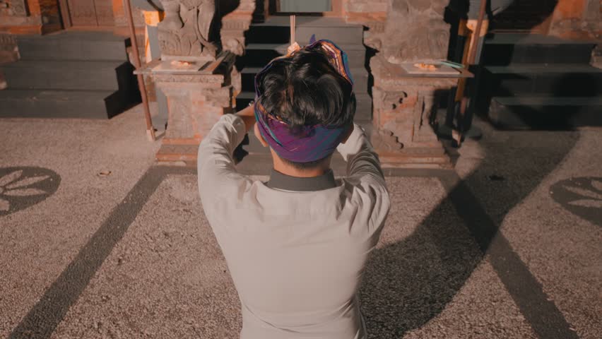 A person with a purple headscarf and gray shirt is seen from behind, taking a photo of stone sculptures in a dimly lit area.