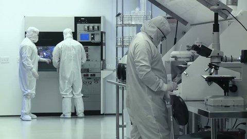 Clean Room Wide. Scientists / technicians working on silicon chip manufacture in a clean room, wearing full body white "bunny suit" coveralls to avoid contamination.  Wide view.