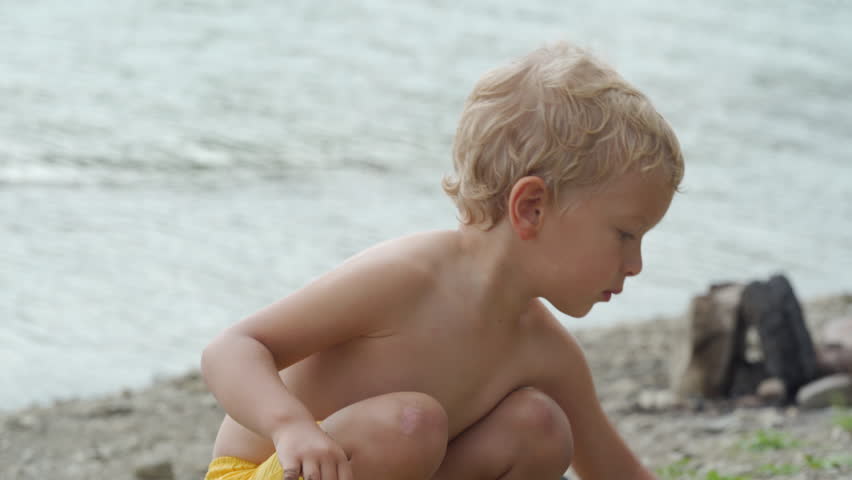 Small child playing on lake shore on summer day. Little boy playing with toy excavator