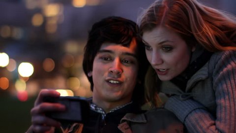Smart Phone Couple at Night.  Attractive young couple laugh as they find content on a smart phone which illuminates their faces as day turns to night.