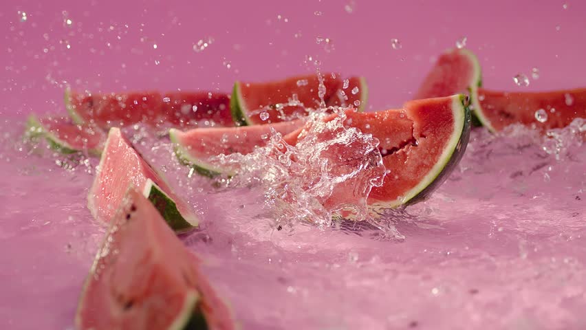 Many pieces of sliced watermelons falling , dropping on water in pink background . Slices of watermellon fall on the floor . Water splashing . Slow motion . Fresh and healthy food . Beautiful scene  