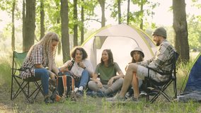 A joyful group of friends enjoying a delicious dinner in a lunch box and tea in a thermos on a camping trip, sharing stories and laughter while sitting next to the tents. - Powered by Shutterstock - Get 15% off with code: PIKWIZARD15