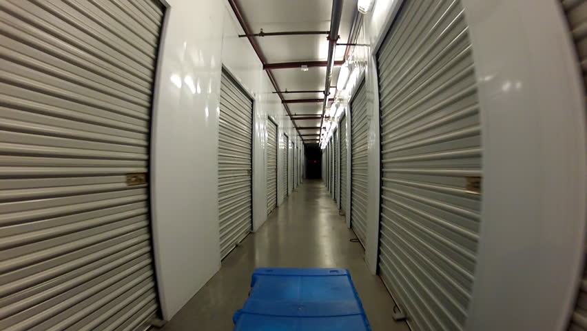 A camera mounted on a dolly behind a footlocker rolls down a long corridor past