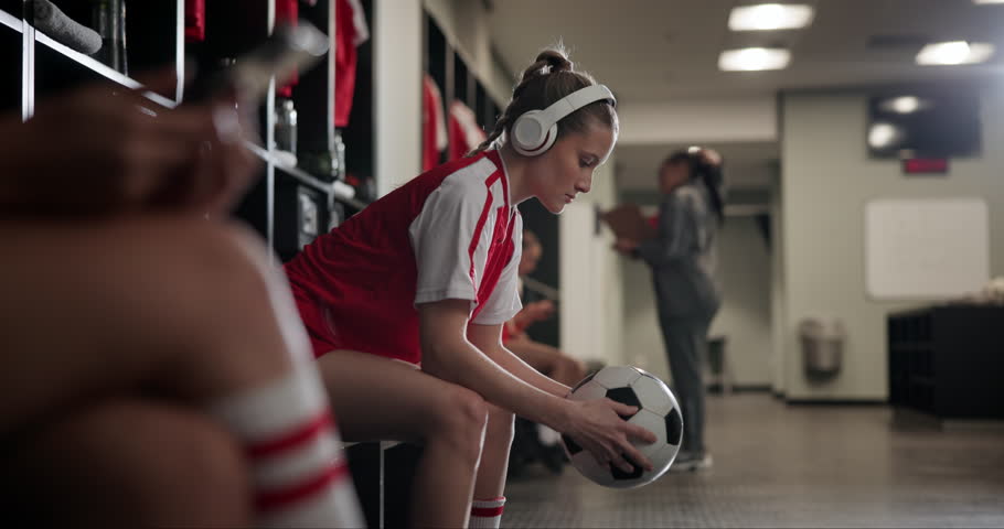 Girl, soccer and headphones with ball in locker room for preparation or getting ready with team for game. Female person or sports player with earphones and waiting in half time for next match or play