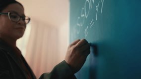 Concentrated Asian woman teacher writing math equation on chalkboard in class - Powered by Shutterstock - Get 15% off with code: PIKWIZARD15