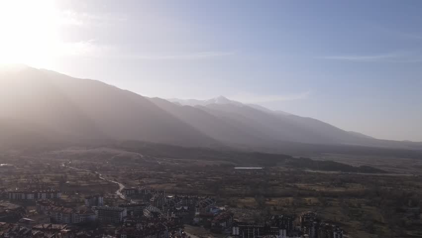 Experience the breathtaking beauty of a mountain landscape as the sun sets over a tranquil valley. The view captures rolling hills, distant peaks, and a peaceful town nestled below.