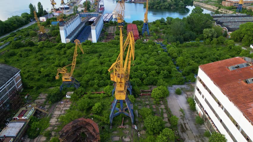 Dilapidated abandoned port cranes, dry dock and infrastructure at the Danube river port of Ruse in Bulgaria. Drone shot of graving dock with ship to shore cranes on the bank of a river. STS crane.