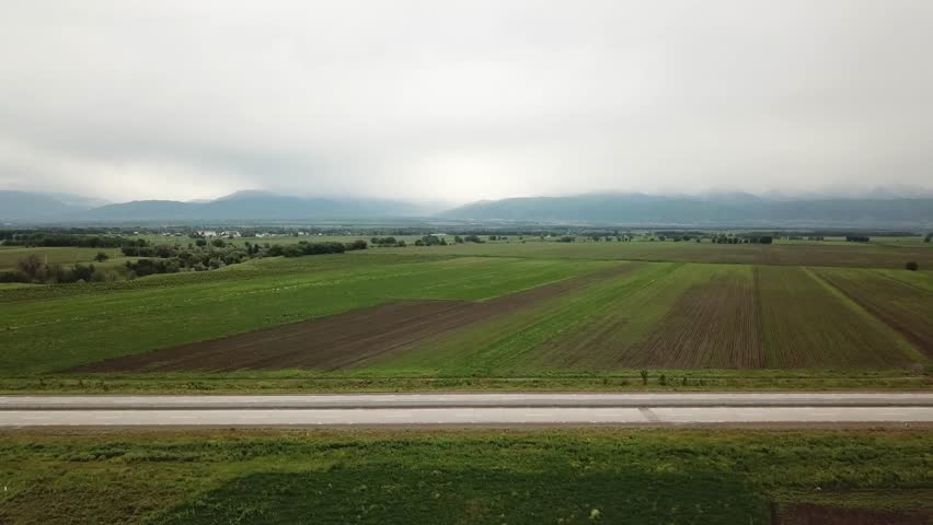 A white car driving on a high-speed highway among green fields and mountains on a cloudy day. Road with concrete pavement. Almaty-Khorgos highway in Kazakhstan