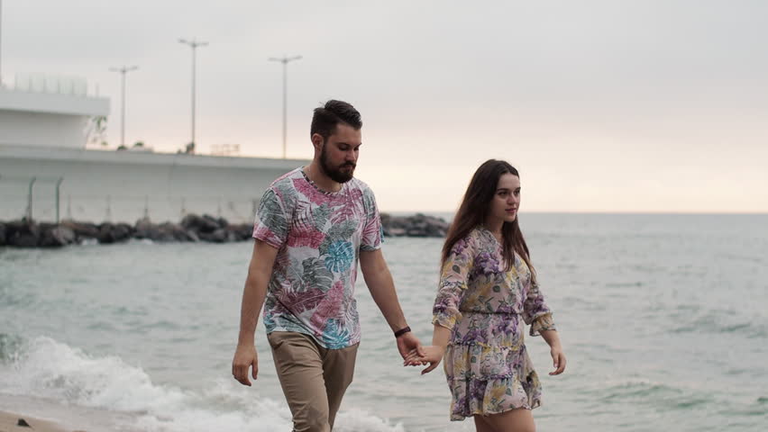 Date at sea at dawn. Lovers walk along the beach. They hug and kiss.