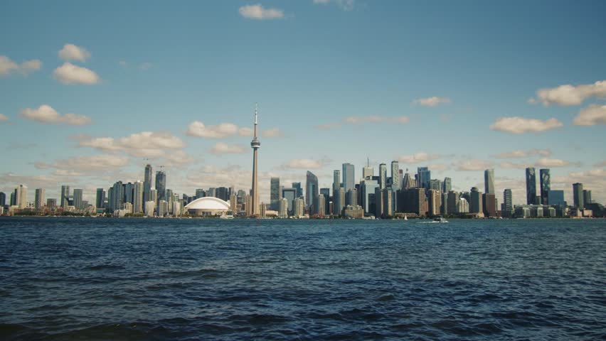 Clear day view of Toronto cityscape from an island on Lake Ontario. The CN Tower and skyscrapers stand tall against the blue sky. Toronto Iconic Skyline from Lake Ontario Island 