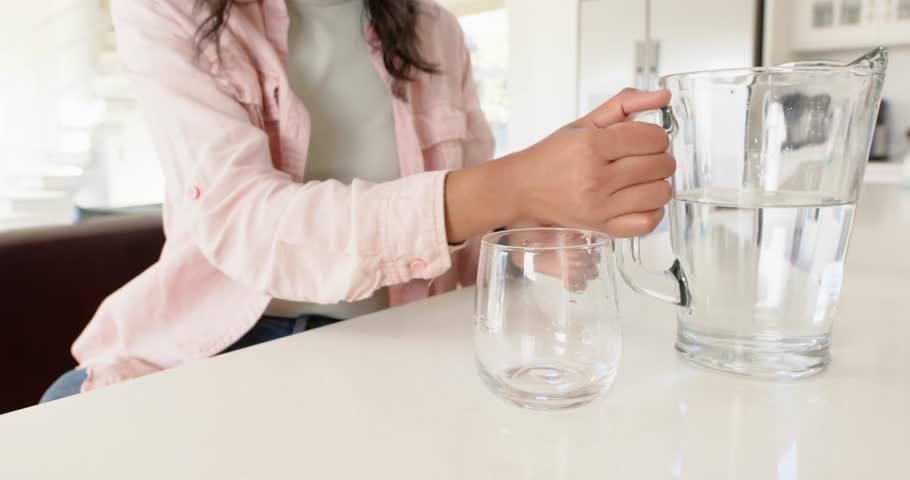 Lifestyle videos indoor of people doing activities at home, drinking water, woman in casual outfit at home. pouring a liquid into a cup, pouring water in a cup and drinking it