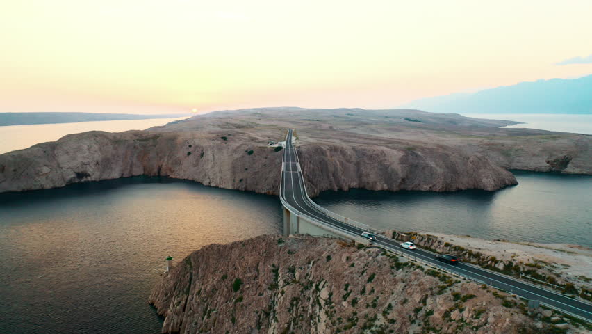 Pag Bridge with driving vehicles over Adriatic Sea channel at sunset. Road network connects island to Croatian mainland offering stunning views