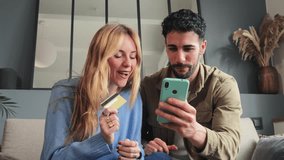 A young couple ordering food online using a delivery app on a mobile phone. Man and woman are sitting on the couch in their house, paying online with a credit card and a cellphone for a trip. High - Powered by Shutterstock - Get 15% off with code: PIKWIZARD15