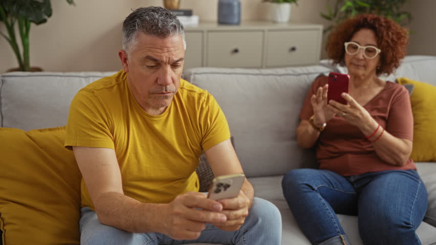 Middle-aged man and woman using smartphones in a cozy living room showcasing a modern indoor setting.