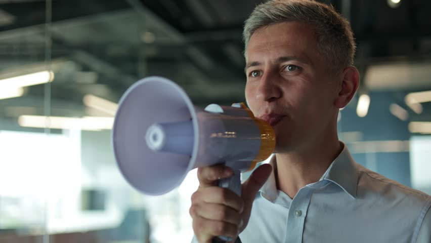Close-up of a businessman talking into a megaphone, making an announcement in the office.