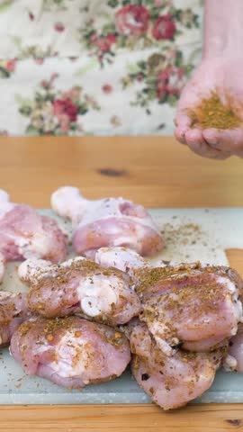 Housewife salting and seasoning raw chicken on a cutting board in the kitchen. Preparing meal at home.