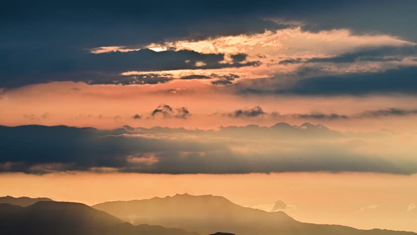 A serene sunset over misty mountains with golden and orange hues. Layered clouds and distant peaks create a tranquil scene. Caoshan, Shuangxi District, Taiwan.