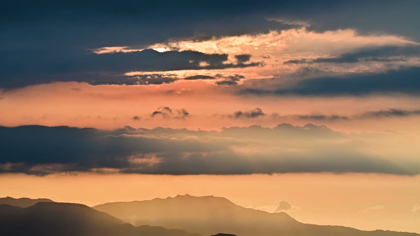 A serene sunset over misty mountains with golden and orange hues. Layered clouds and distant peaks create a tranquil scene. Caoshan, Shuangxi District, Taiwan.