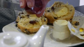 A close-up of a person spreading strawberry jam on a buttered scone, with clotted cream in a jar nearby. The detailed view of the scone. - Powered by Shutterstock - Get 15% off with code: PIKWIZARD15