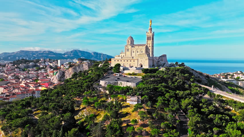 Grand basilica on top of a hill crowned by a golden statue, old city centre and port by blue Mediterranean sea coast in Marseille, France. Basilica of Notre Dame of la Garde at Marseille in France.