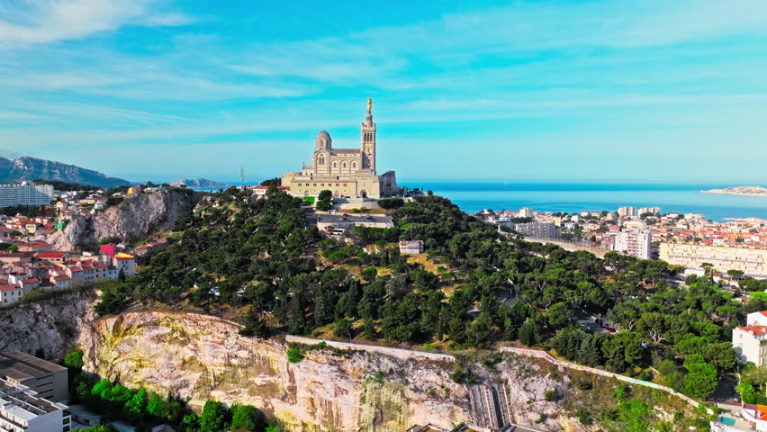 Grand basilica on top of a hill crowned by a golden statue, old city centre and port by blue Mediterranean sea coast in Marseille, France. Basilica of Notre Dame of la Garde at Marseille in France.