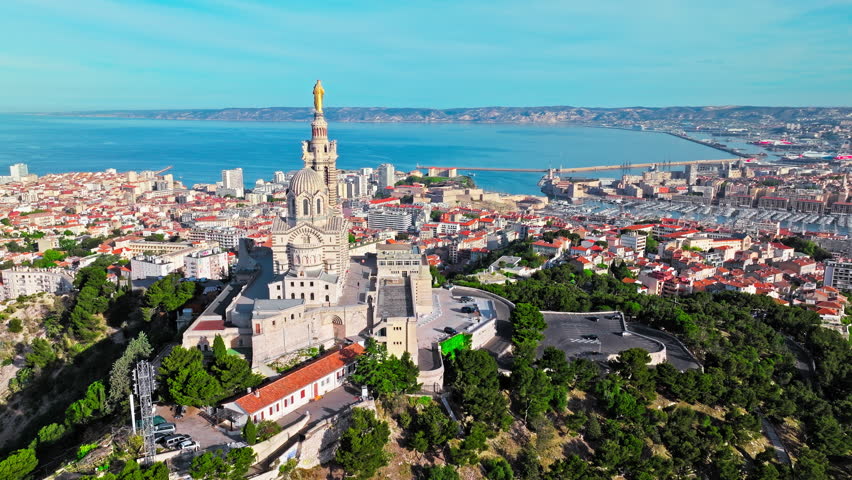 Grand basilica on top of a hill crowned by a golden statue, old city centre and port by blue Mediterranean sea coast in Marseille, France. Basilica of Notre Dame of la Garde at Marseille in France.
