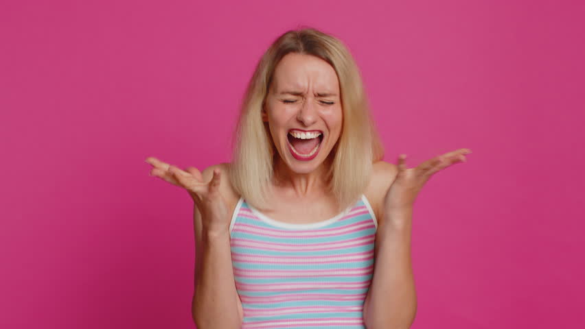 Irritated angry Caucasian young woman 30 years old screams from stress tension problems feels horror hopelessness fear surprise shock expresses rage nervous, quarrel. Girl isolated on pink background